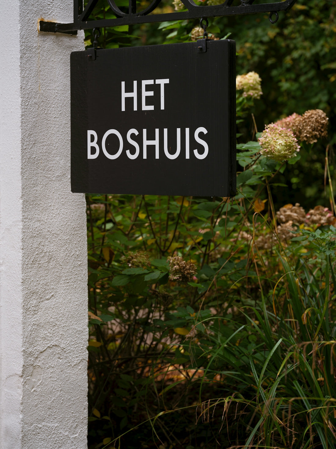 A black sign reads het boshuis with foliage behind it